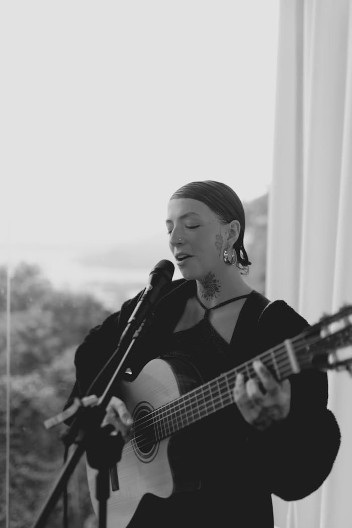 Artistic black and white portrait of a woman singing and playing guitar in a serene setting.
